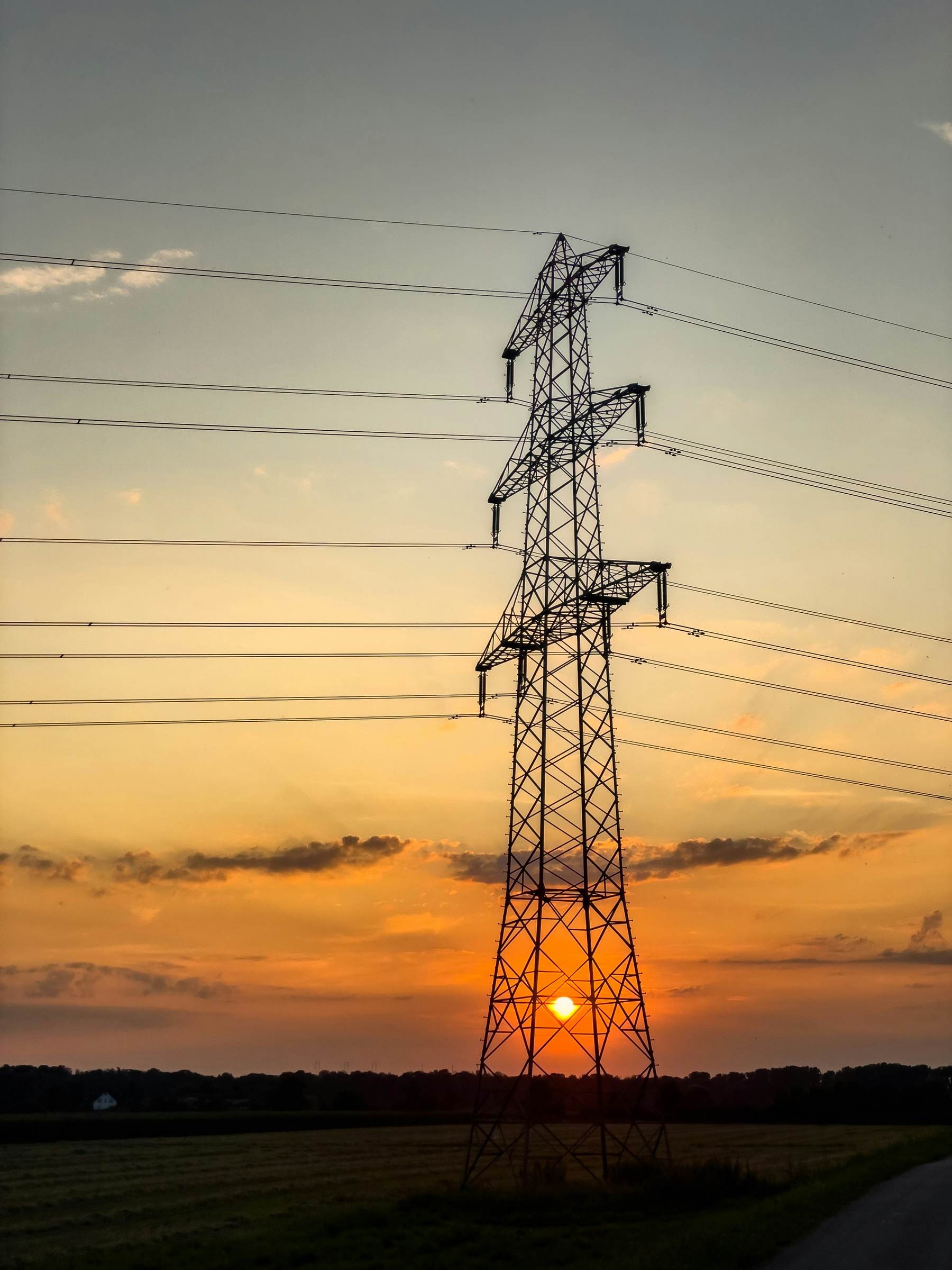 A high-voltage transmission tower silhouetted against a sunset sky