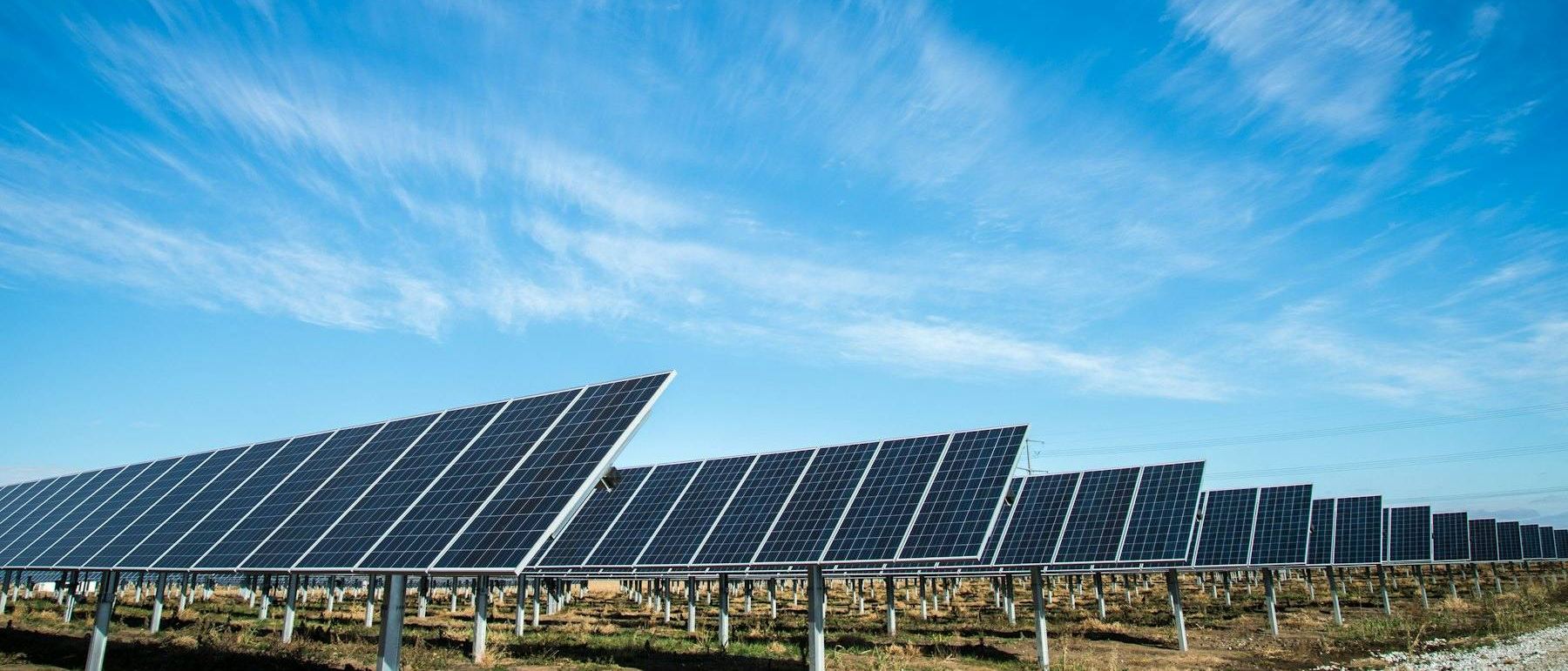 Solar panels angled skyward against a dramatic blue sky with wispy clouds